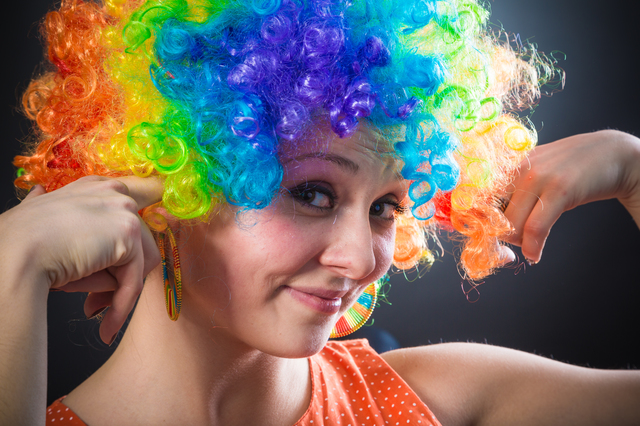 Íoung beauty woman in multicolored clown wig smiling on black background
